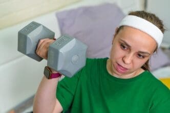 A young woman in a fitness studio lifts a dumbbell while focusing on strength training.
