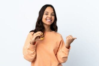 A young woman with long hair holds colorful French macarons and points to the side.