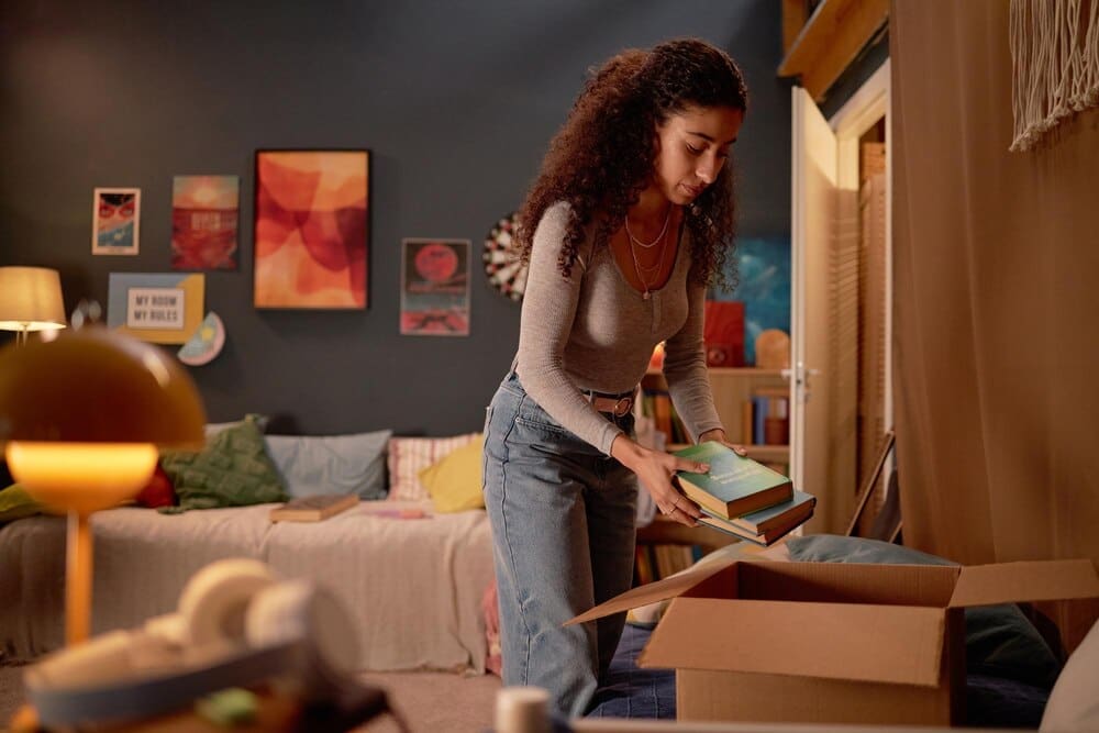 A young woman sorts books on shelves in a comfortable, well-lit room.