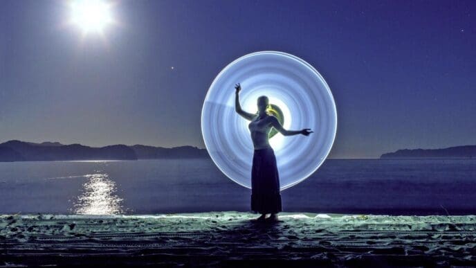 A young woman poses in front of a light painting on a beach at night.