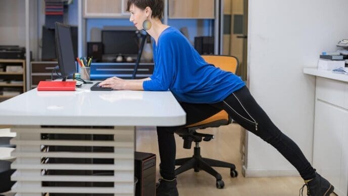 A young woman stretches her arms overhead in an office setting.