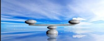 Three smooth, gray zen stones are stacked in a tower against a backdrop of a bright blue sky and ocean.