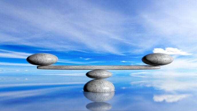 Three smooth, gray zen stones are stacked in a tower against a backdrop of a bright blue sky and ocean.