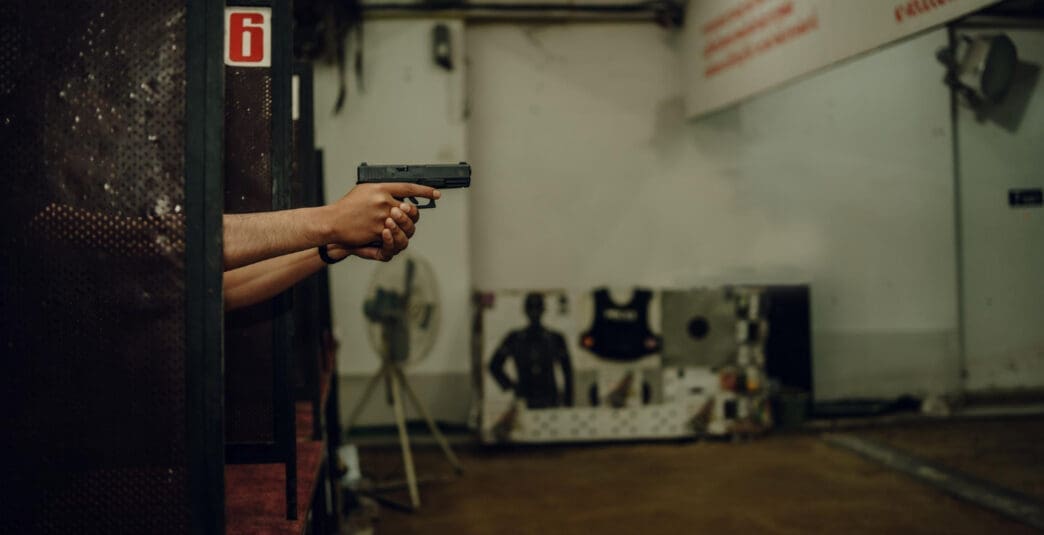 A person holds a pistol with both hands, aiming at a shooting target down range