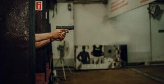 A person holds a pistol with both hands, aiming at a shooting target down range