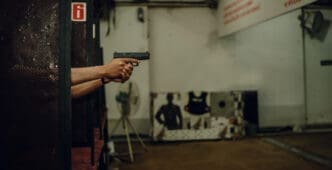 A person holds a pistol with both hands, aiming at a shooting target down range
