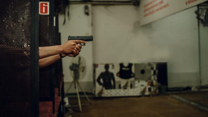 A person holds a pistol with both hands, aiming at a shooting target down range