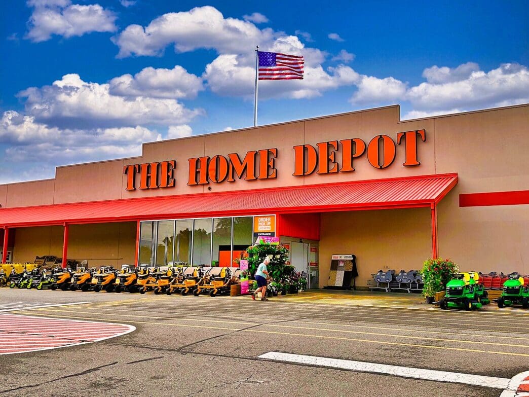 The exterior of a Home Depot store in Blairsville, Georgia, with an American flag flying on the roof and riding lawnmowers in the foreground.