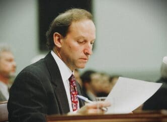 A man in a suit and tie, Abbe D. Lowell, looks down at a document he is holding