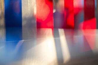 An abstract photograph featuring a blur of vertical bands of red, white, and blue light against a gray background.