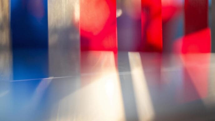 An abstract photograph featuring a blur of vertical bands of red, white, and blue light against a gray background.