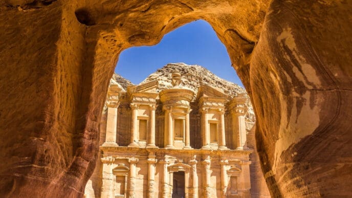 The Monastery (Ad Deir) in Petra, Jordan, is seen from a cave opening, with the ancient building carved into the rock face.