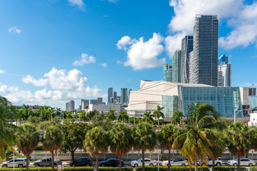 A wide view of the Adrienne Arsht Center for the Performing Arts in Miami, a modern complex of buildings with glass facades and palm trees in front of a skyline of skyscrapers.