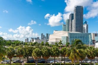 A wide view of the Adrienne Arsht Center for the Performing Arts in Miami, a modern complex of buildings with glass facades and palm trees in front of a skyline of skyscrapers.