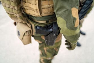 A close-up, high-angle view of an armed National Guard soldier in a camouflage uniform, with a handgun holstered on their right hip.