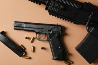 A top-down view of a black pistol, a rifle, a magazine, and several loose bullets on a tan surface