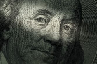 A close-up, macro photograph of Benjamin Franklin's face on a US hundred-dollar bill, with a shallow depth of field focusing on his eyes.