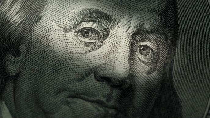 A close-up, macro photograph of Benjamin Franklin's face on a US hundred-dollar bill, with a shallow depth of field focusing on his eyes.