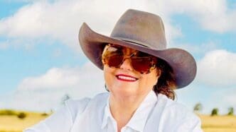 A smiling portrait of Australian billionaire Gina Rinehart wearing a cowboy hat and large sunglasses.