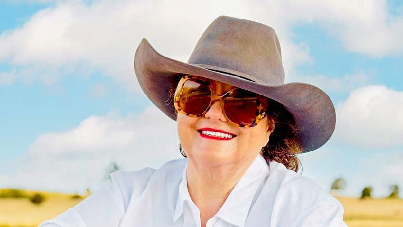 A smiling portrait of Australian billionaire Gina Rinehart wearing a cowboy hat and large sunglasses.