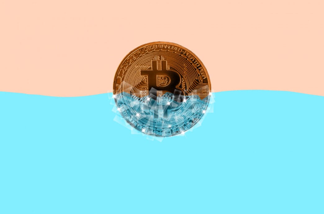 A graphic of a Bitcoin coin half-submerged in water, with a light pink background above the water.