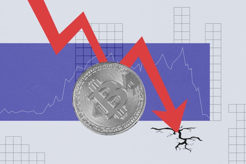 A conceptual illustration of a large red arrow pointing down through a silver Bitcoin coin and cracking the ground, symbolizing a market crash.