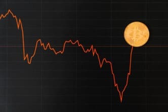 A financial chart shows a sharp downward trend, with a Bitcoin coin placed at the end of the line on the right.