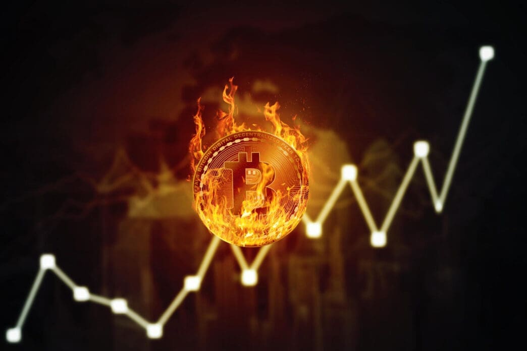 A conceptual image of a Bitcoin coin on fire, placed on a white line graph that shows an upward price trend.