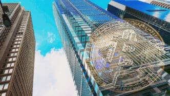 A conceptual image of a large, semi-transparent Bitcoin symbol overlaid on a low-angle photograph of modern glass skyscrapers.