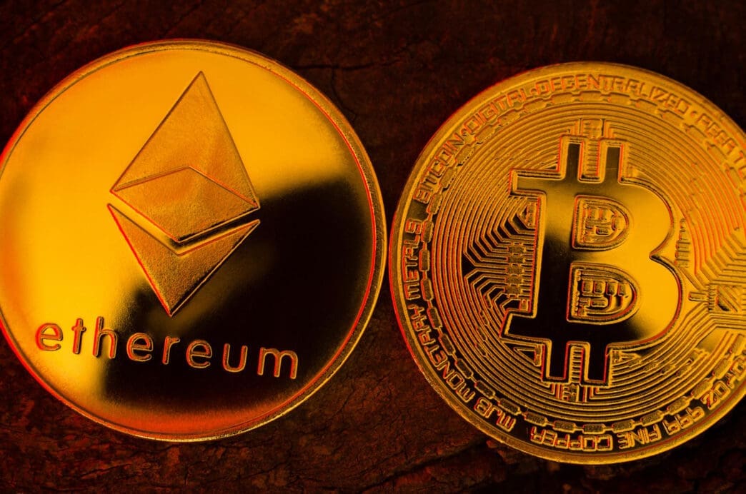 A close-up, macro photograph of a shiny golden Ethereum coin positioned side-by-side with a golden Bitcoin coin.