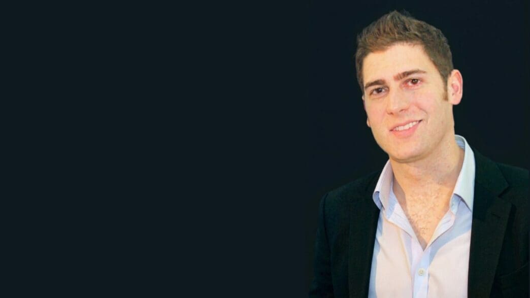 A professional portrait of Brazilian billionaire Eduardo Saverin, smiling and wearing a suit.