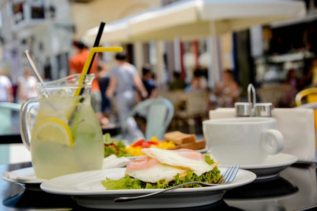 A plate of eggs and lettuce, a pitcher of lemonade, and a coffee cup on a table at a sunny outdoor restaurant.