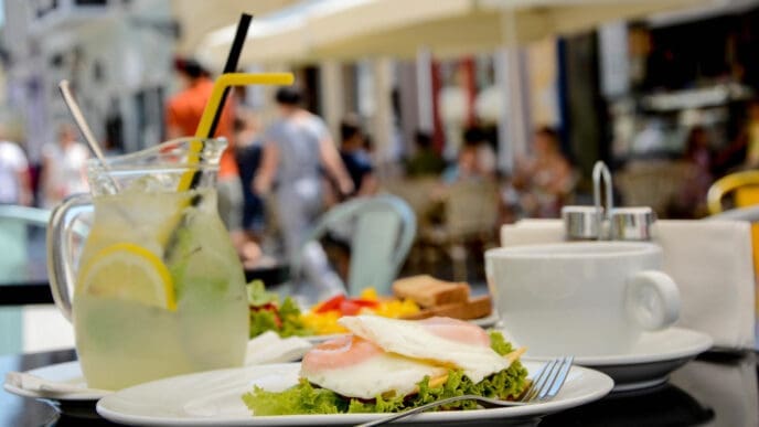 A plate of eggs and lettuce, a pitcher of lemonade, and a coffee cup on a table at a sunny outdoor restaurant.