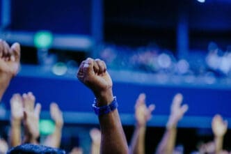 A close-up of a raised fist in a crowd, with a blue wristband, symbolizing solidarity and political action.