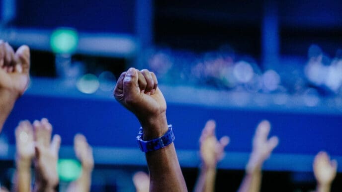A close-up of a raised fist in a crowd, with a blue wristband, symbolizing solidarity and political action.