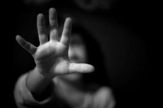 A black and white photograph of a child's hand reaching out with the palm facing the camera, while their face is blurred and out of focus in the background.