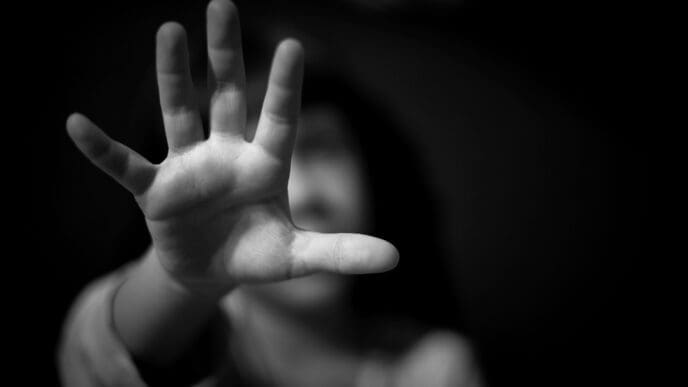 A black and white photograph of a child's hand reaching out with the palm facing the camera, while their face is blurred and out of focus in the background.