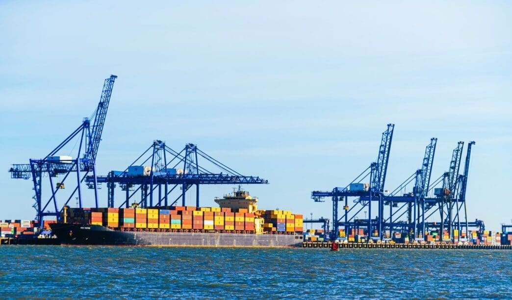 A large container ship is being unloaded at a port by several blue industrial cranes