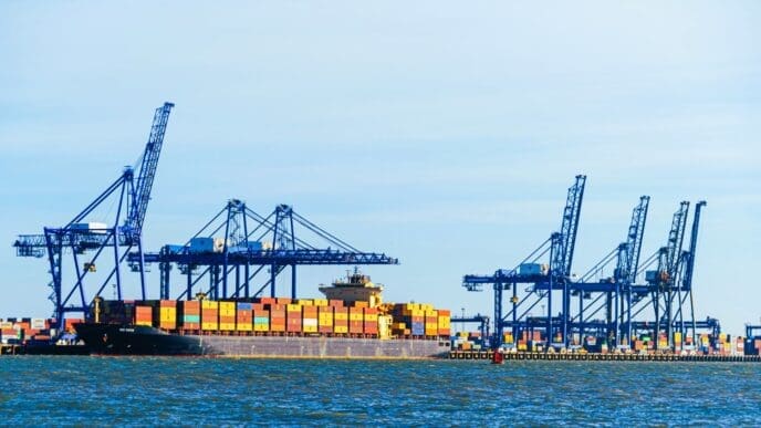 A large container ship is being unloaded at a port by several blue industrial cranes