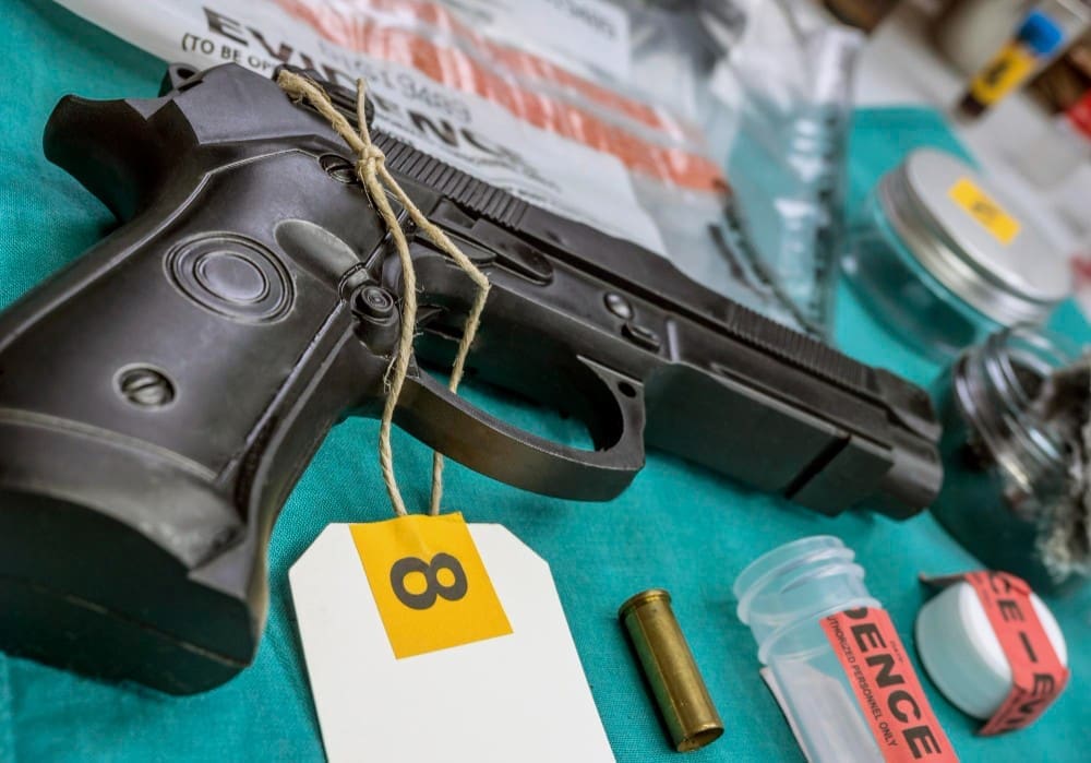 A handgun with an evidence tag and a single bullet casing are laid out on a table, representing forensic evidence.