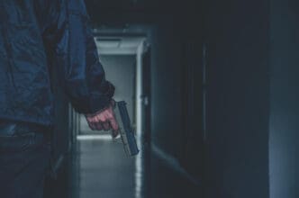 A person wearing a dark jacket holds a handgun in a dimly lit hallway