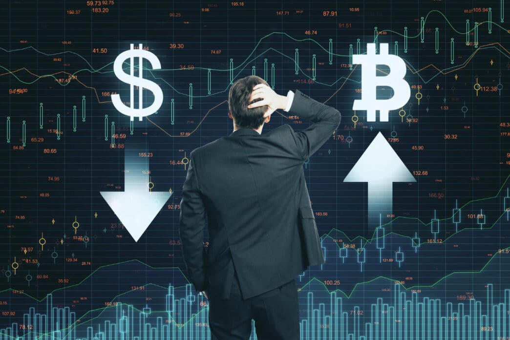 A man in a suit scratches his head while looking at a complex digital screen with financial charts. In front of him, a large dollar sign points down, while a large Bitcoin symbol points up.