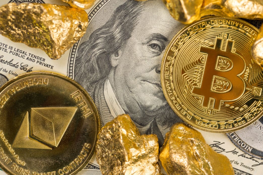 A close-up photograph showing a US hundred-dollar bill with a Bitcoin coin, an Ethereum coin, and several gold nuggets placed on top of it.