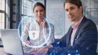 A man and a woman are seated at a table with a laptop, with a glowing digital overlay of a padlock icon and a circular network, symbolizing a discussion about cyber security or data protection.