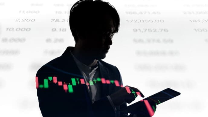 The silhouette of a person in a suit is shown looking at a tablet, with a glowing financial candlestick chart overlaid on both the tablet and their body.