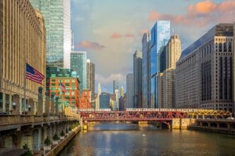 The Chicago River runs through the city, with a red metal bridge and an elevated train crossing it, surrounded by a dense skyline of skyscrapers.