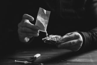 A person's hands pour a white powder from a small bag onto a piece of foil