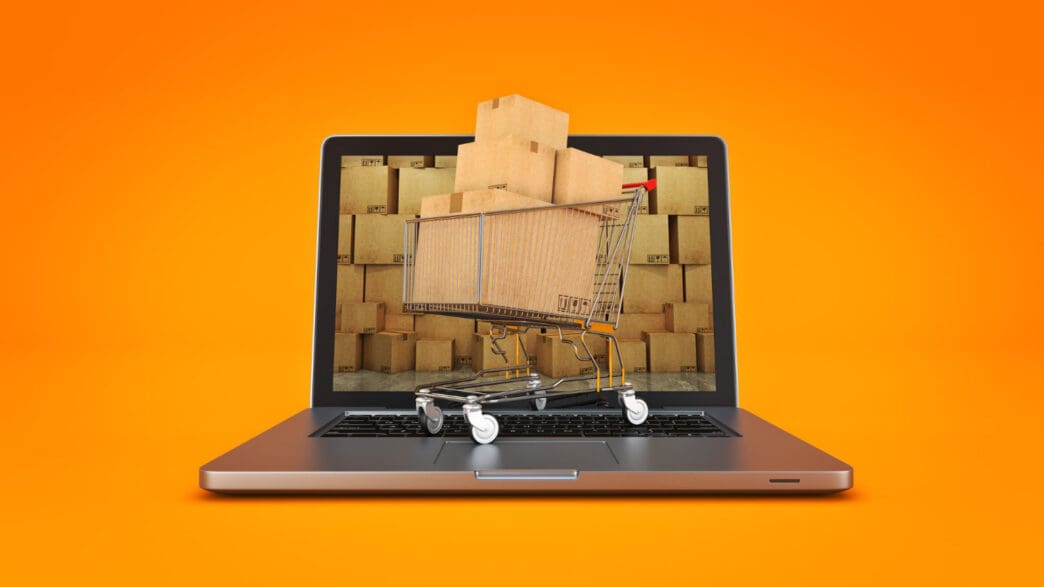 A shopping cart full of boxes on a laptop screen with a background of more boxes.