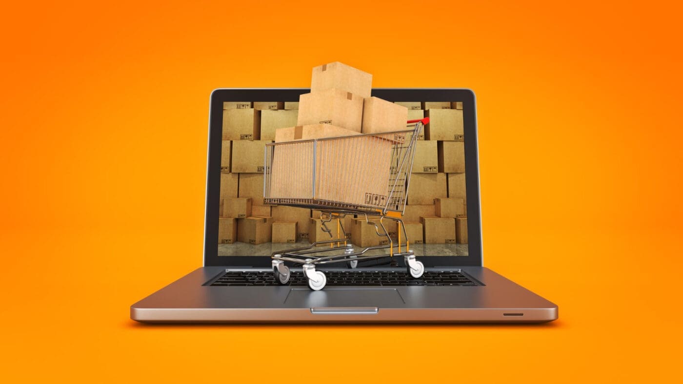 A shopping cart full of boxes on a laptop screen with a background of more boxes.