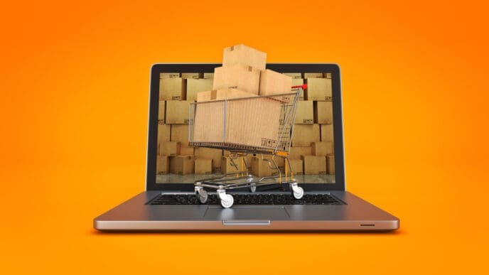 A shopping cart full of boxes on a laptop screen with a background of more boxes.